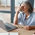 Overworked older woman sitting at a work desk with a laptop