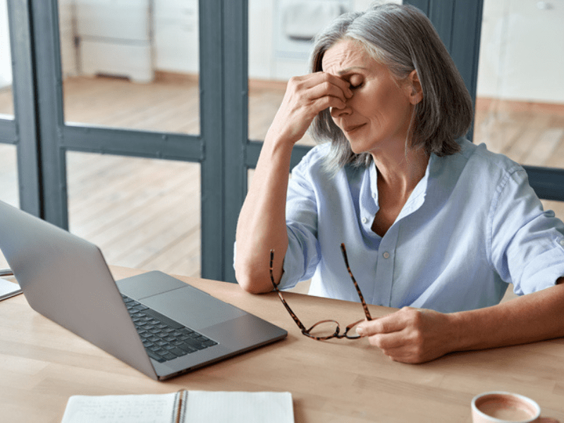 Overworked older woman sitting at a work desk with a laptop