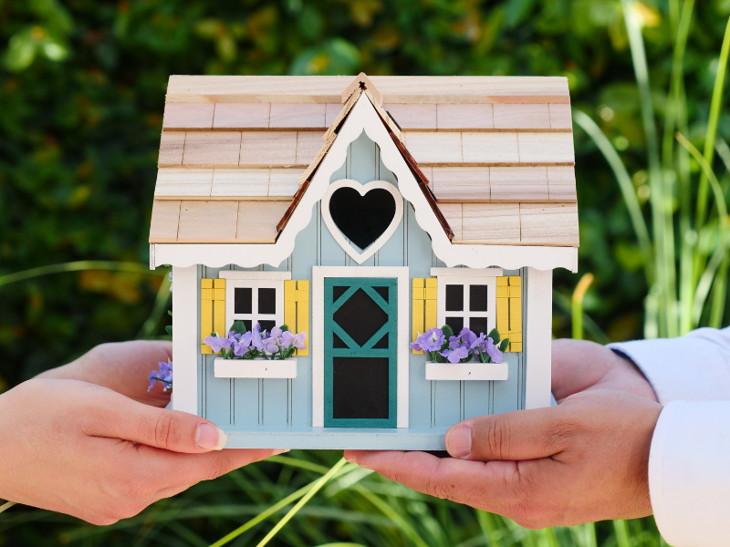 People holding miniature wooden house