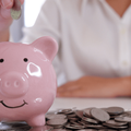 Person inserting coin in pink Piggybank