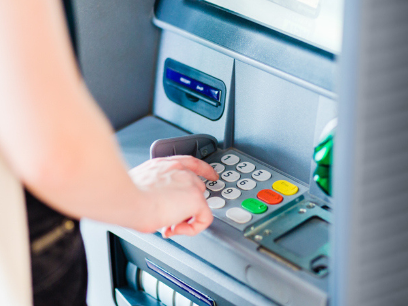 Person entering pin code using atm bank machine