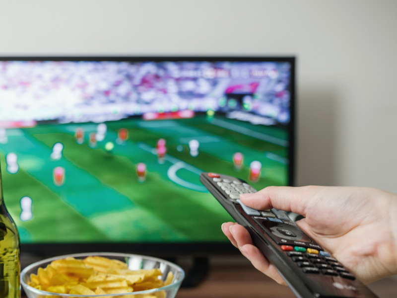 Person holding a TV remote and watching football