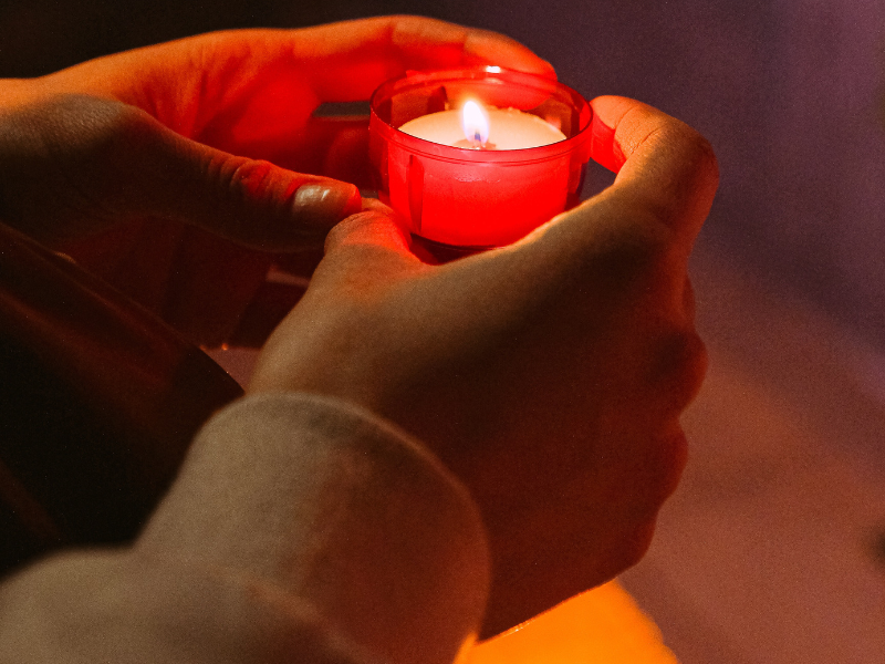 Person holding a red candle in a dark room