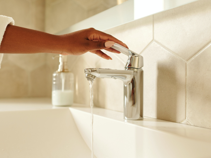 Person holding stainless steel faucet with minimal flow of water running from tap