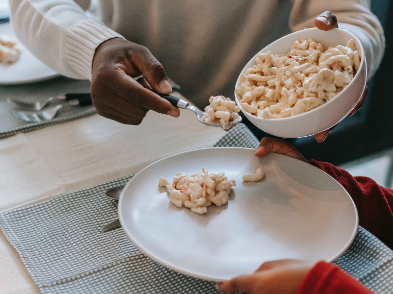 Person serving up macaroni and cheese for a kid