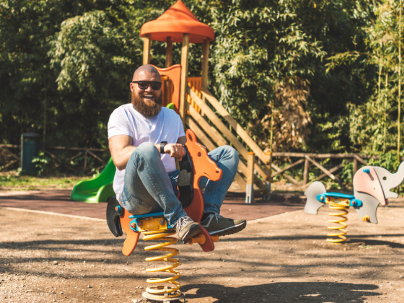 Playful crazy man riding wooden rocking horse in playground