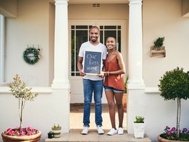 Portrait of a young couple holding a chalkboard with our first home written on it
