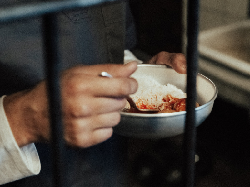 Prisoner holding a bowl with food in jail cell