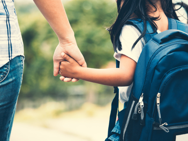 Pupil with backpack holding her mother's hand