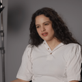 Rosalía wears a white top while sitting in a studio