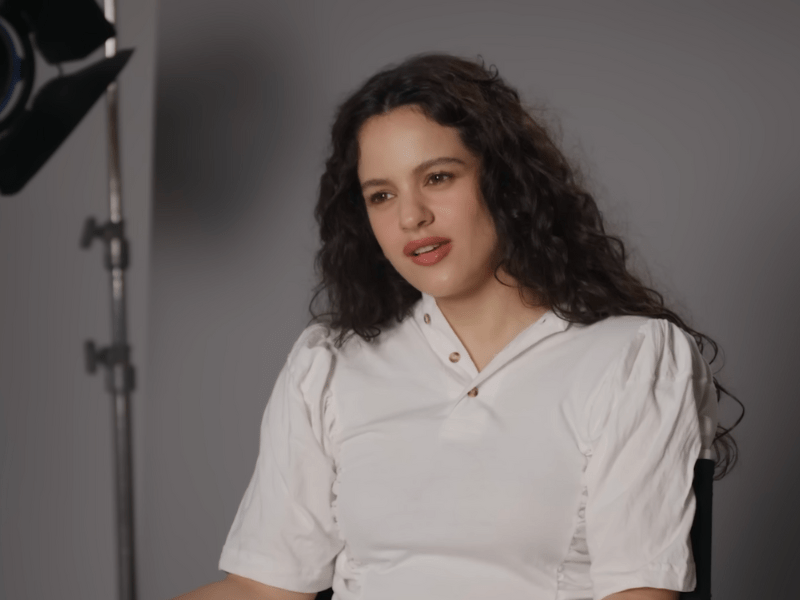 Rosalía wears a white top while sitting in a studio