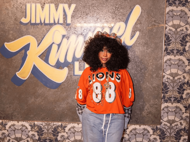 SZA wearing an orange sports jersey and light blue jeans