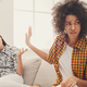 Two female friends sitting on sofa and arguing istock