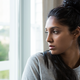 Thoughtful young woman by window istock