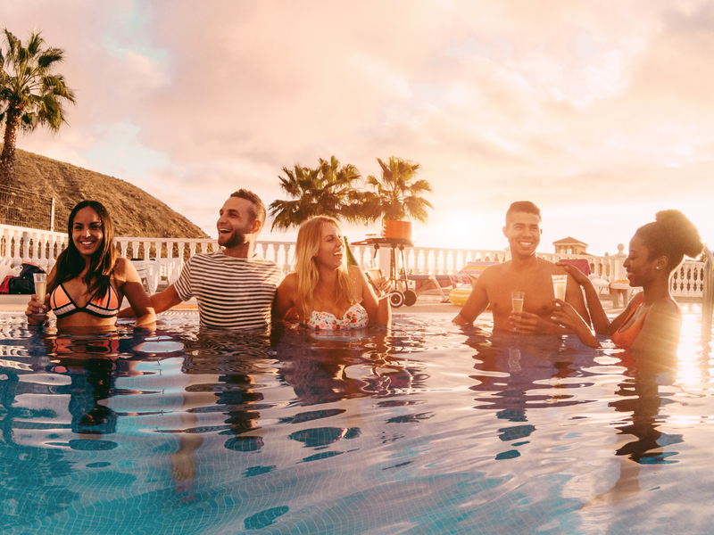 Happy friends drinking champagne in pool party at sunset / iStock