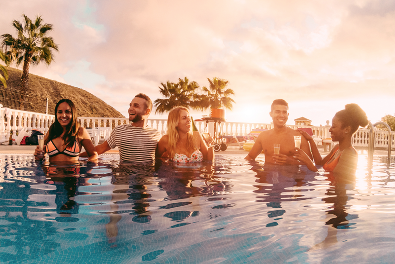 Happy friends drinking champagne in pool party at sunset / iStock