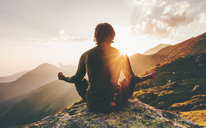 Man meditating yoga at sunset mountains / iStock