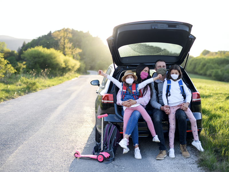 Front view of family with two small daughters on trip outdoors in nature, wearing face masks.