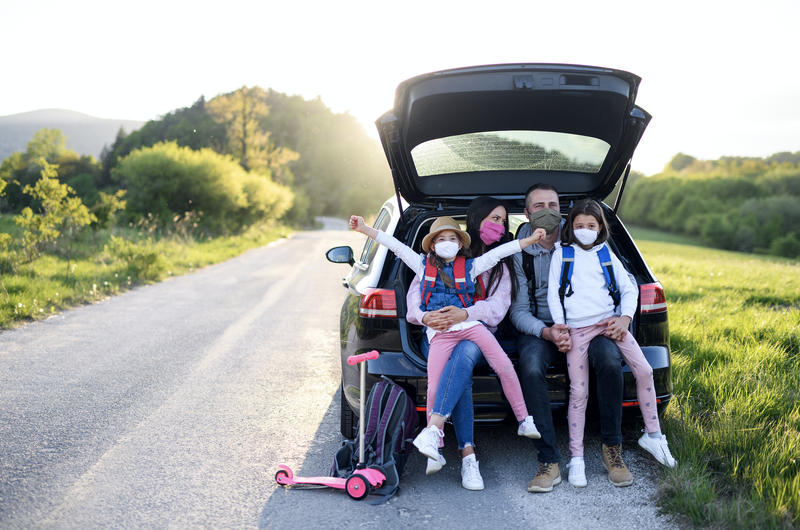 Front view of family with two small daughters on trip outdoors in nature, wearing face masks.