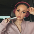 Selena Gomez sits in a car while wearing maroon headphones