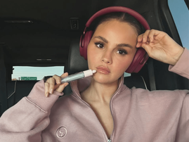 Selena Gomez sits in a car while wearing maroon headphones