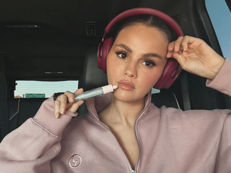 Selena Gomez sits in a car while wearing maroon headphones