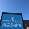 An advertisement billboard reading 'Welcome to Shamchester' in Manchester