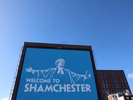 An advertisement billboard reading 'Welcome to Shamchester' in Manchester