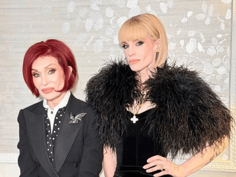 Sharon and Kelly Osbourne posing against a light wallpaper backdrop