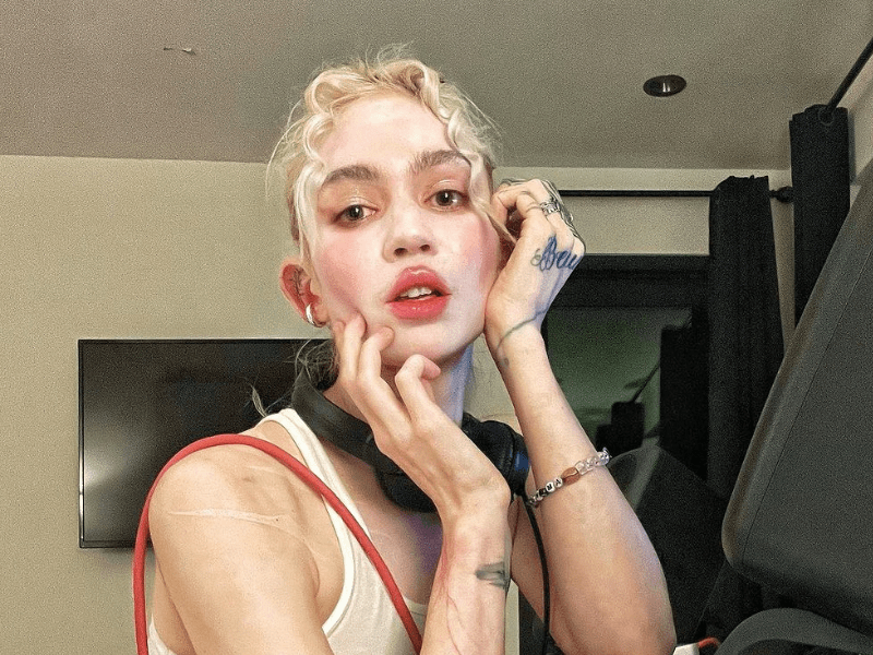 Singer Grimes wearing a white tank top and headphones around her neck