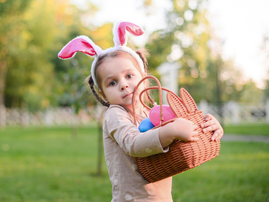 Girl wearing bunny ears holds an Easter basket outdoors