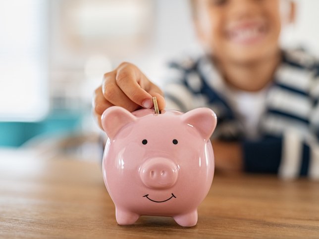 Smiling child saving money in piggybank