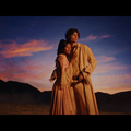 sombr embraces a woman while posing in an open landscape at dusk