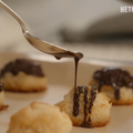 Spoon drizzles chocolate over coconut macaroons on a baking tray