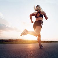 Sporty woman running at sunset on the road
