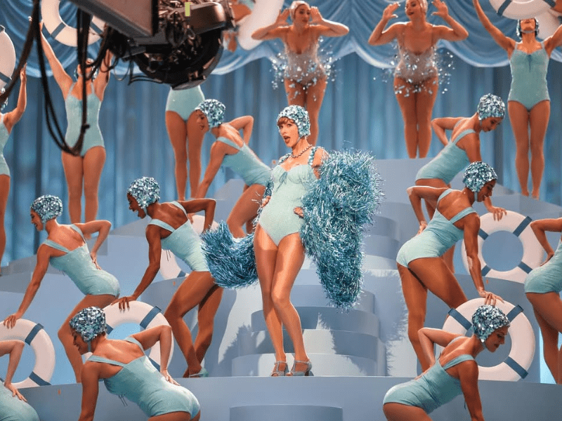 Taylor Swift and dancers wear matching blue costumes and glittering swim cap
