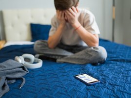 Teenager feeling sad after reading bad news on mobile phone in bedroom