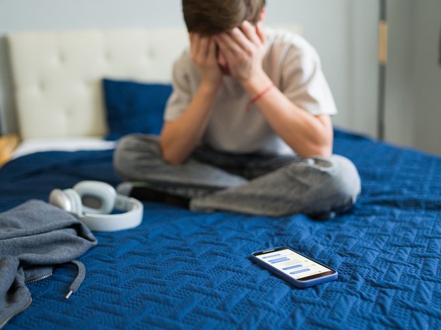 Teenager feeling sad after reading bad news on mobile phone in bedroom