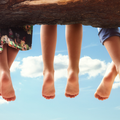 Three children sitting on a tree branch tangling their feet