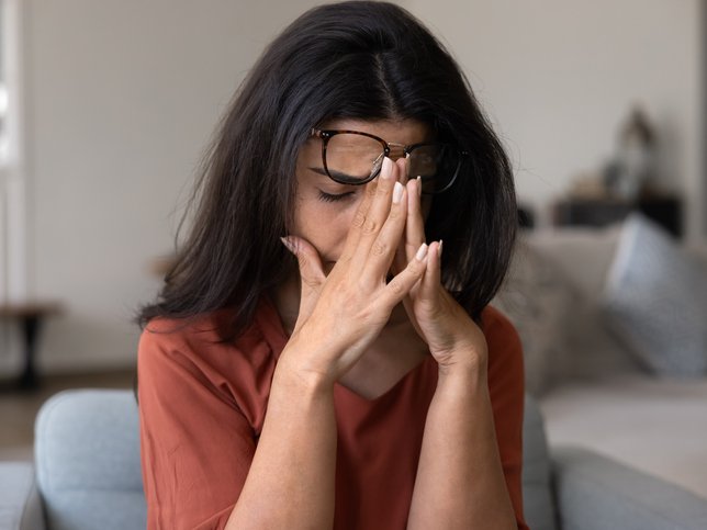 Tired woman removing glasses from closed eyes