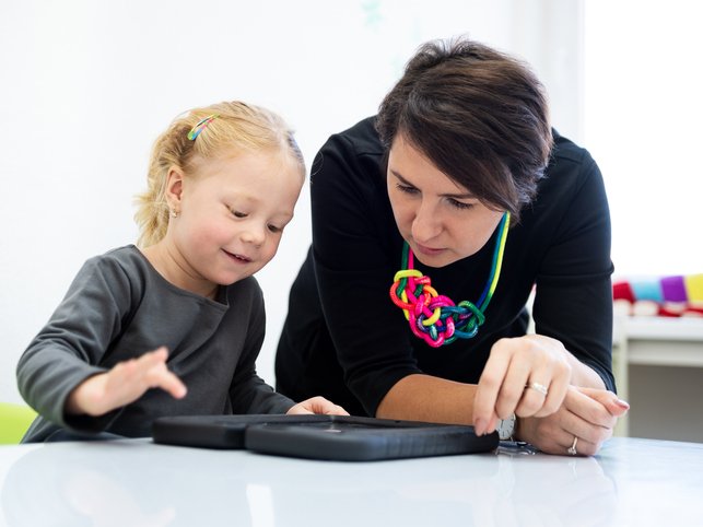 Toddler girl in child occupational therapy session doing playful exercises on a digital tablet with her therapist