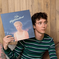 Troye Sivan sits on a couch while holding vinyl