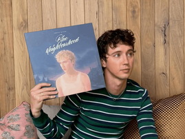 Troye Sivan sits on a couch while holding vinyl