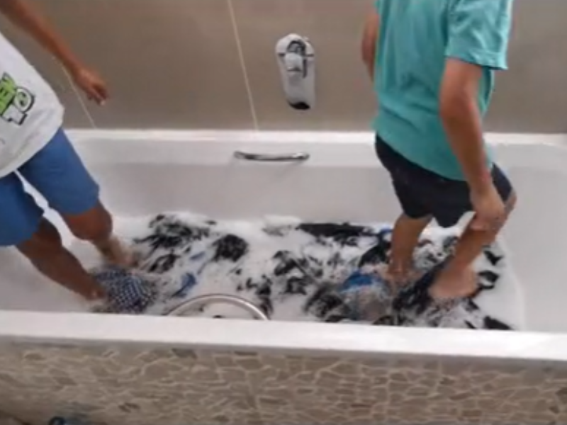 Two boys washing clothes with their feet in a bathtub