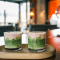 Two glasses of matcha and berry lattes served on a wooden tray