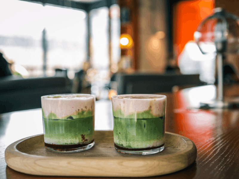 Two glasses of matcha and berry lattes served on a wooden tray