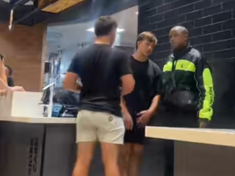Two guys stand inside a McDonalds restaurant talking to a security guard