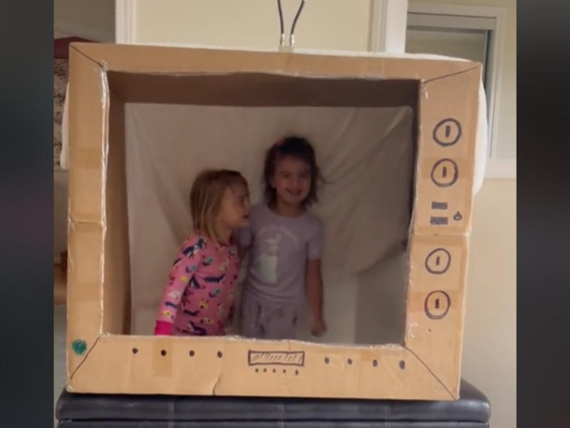 Two kids inside a cut out box that is a play TV