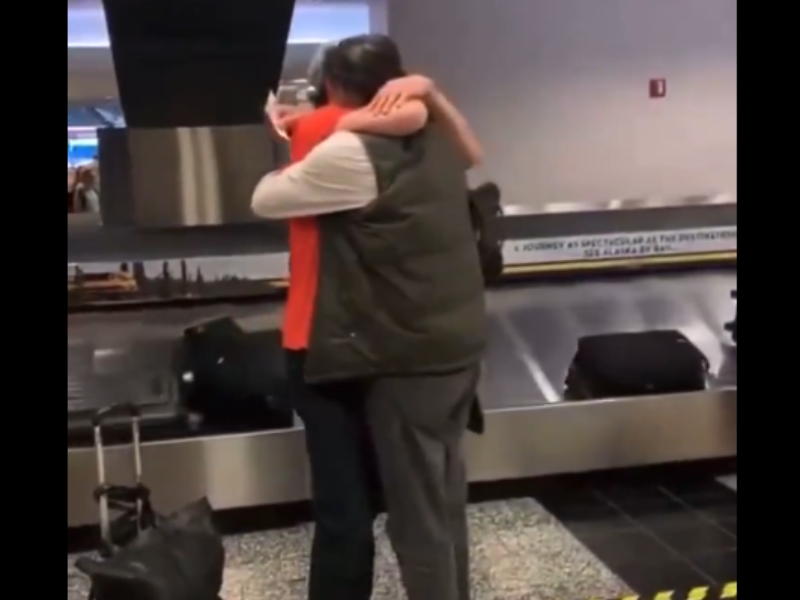 Two men hug at the airport baggage claim carousel