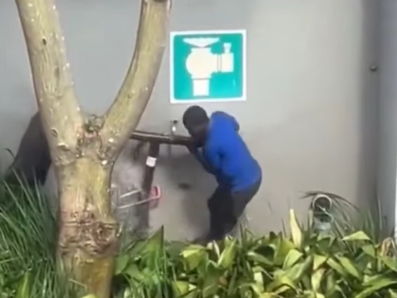 Two men illegally remove a steel water pipe from a fitting on a building